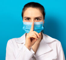 doctor puts her finger to her mouth to say shhhh, don't report medical mistake