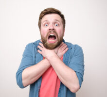Frightened bearded man clutches his throat because of angioedema