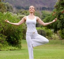 woman in park balances on one leg in yoga stance
