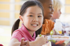 three young children eating lunch with vegetables