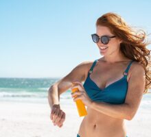 woman spraying sunscreen at the beach